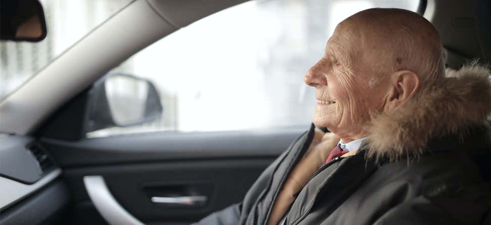A senior male is riding in a Lyft, smiling on his way to his destination.