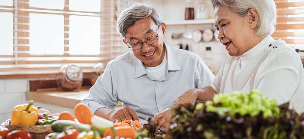 A senior Asian couple in the kitchen is cooking with fresh produce.