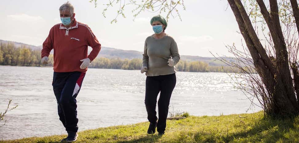 Senior couple wearing masks during COVID pandemic goes for a jog by the river.