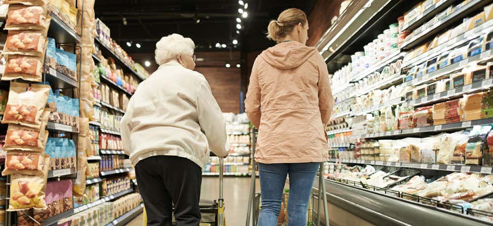 A senior Caucasian woman and her female caregiver are shopping for groceries.
