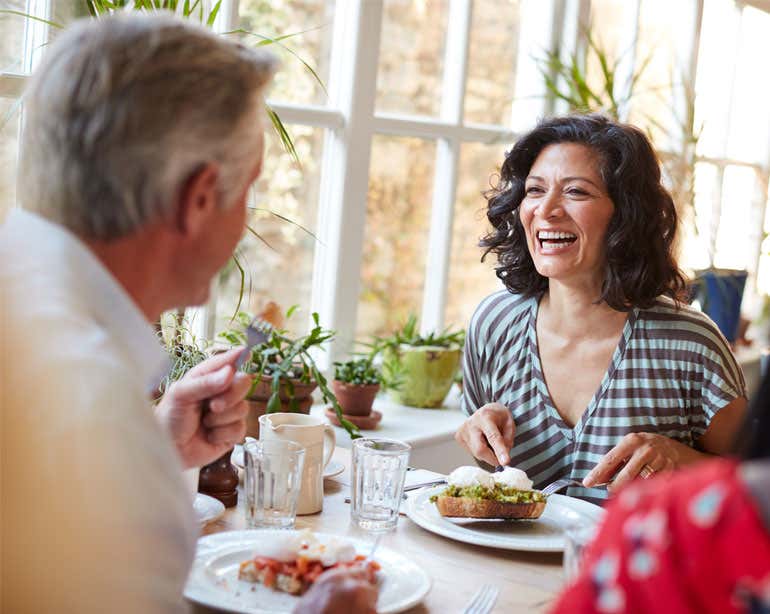 A middle-aged woman is enjoying her brunch with her father, laughing during their conversation.