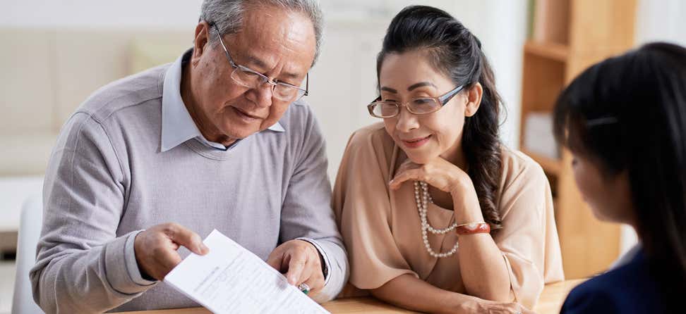 A senior Asian couple is looking over a financial document with their benefits enrollment advisor.