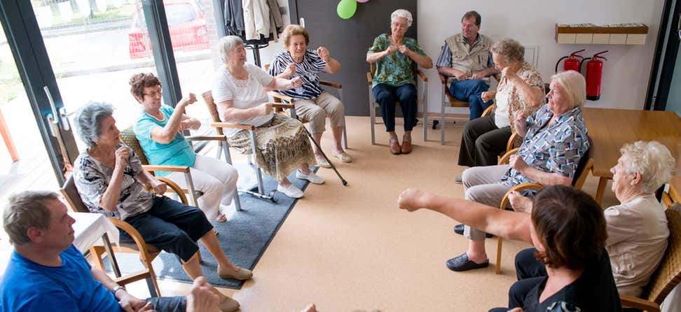 A group of seniors are doing exercises while seated at a senior center.