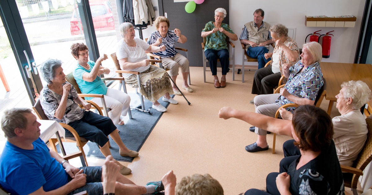 A group of seniors are doing exercises while seated at a senior center.