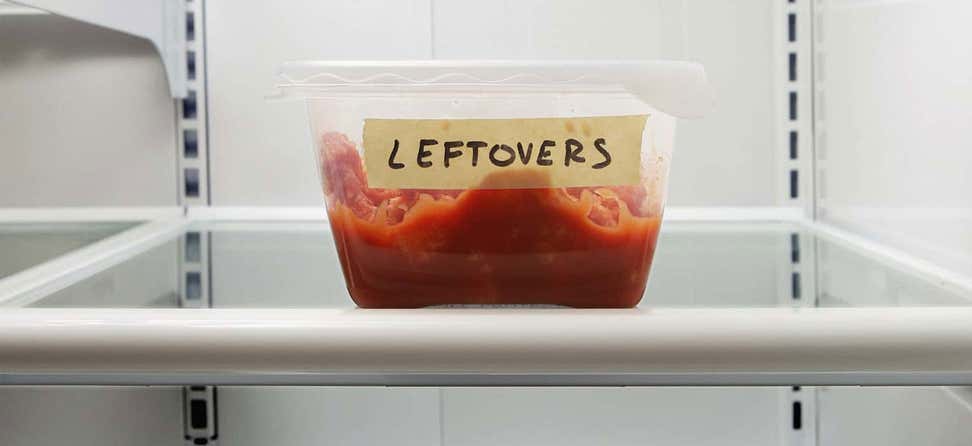 Closeup shot of a food container in a fridge that is labeled as "leftovers" with masking tape.