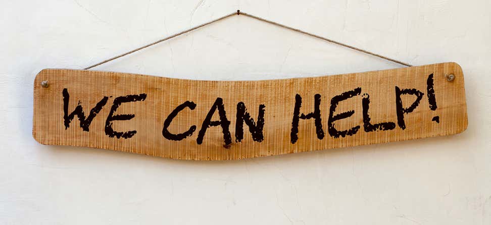A hanging wooden sign with the phrase "We can help!" written on it. 