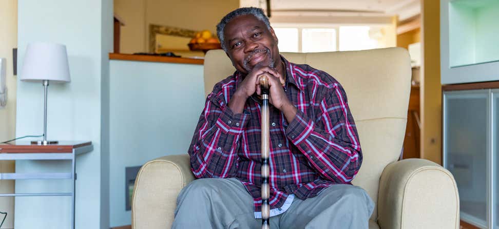 A Black senior man is sitting at home in a comfortable chair, smiling.