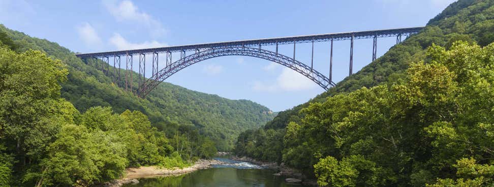 A beautiful, scenic picture of a massive steel bridge surrounded by mountains and a stream running underneath.