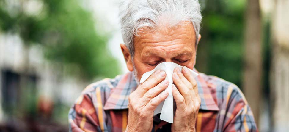 A senior Hispanic man is sneezing into a tissue, indicating that he has the common cold.