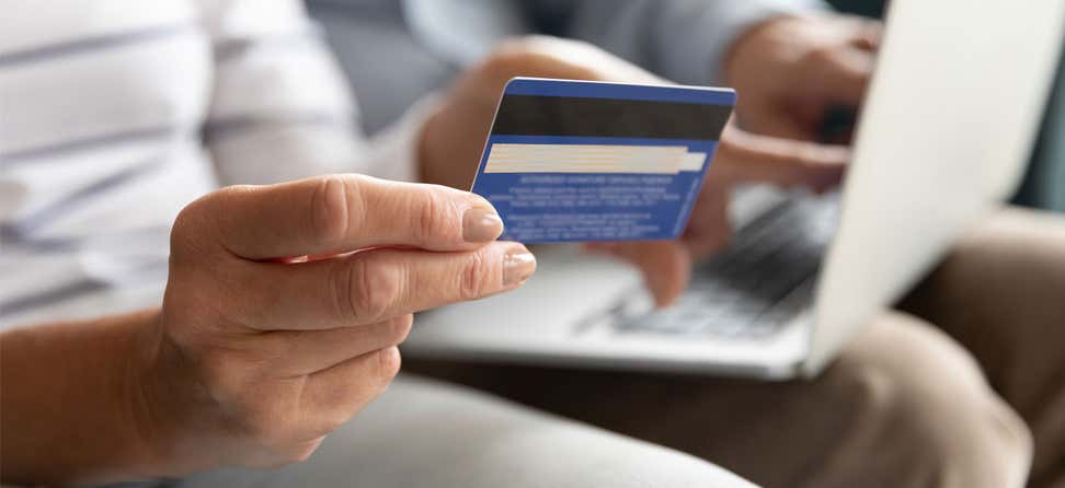 A closeup shot of a wife holding her credit card while her senior husband has the laptop ready for payment.