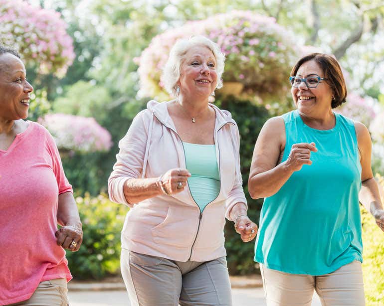Three senior women are exercising together outside.
