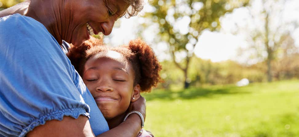 A close up of a Black senior woman hugging her granddaughter in the park.