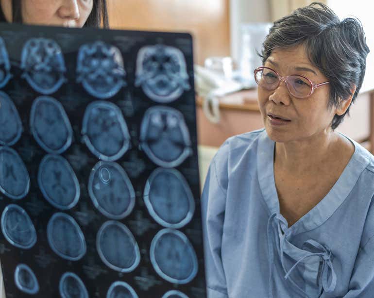 A senior Asian woman looks at Magnetic Resonance Imaging (MRI) film for neurological medical treatment with her doctor.