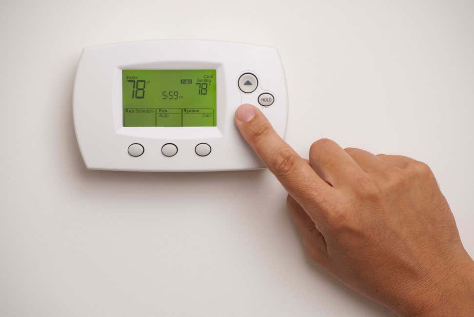 Hand pointing to digital thermostat on wall
