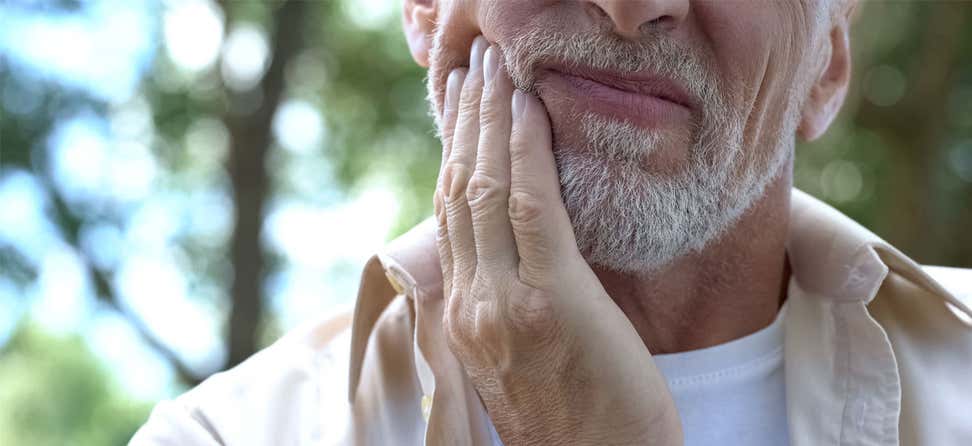 An older man is seen placing his hand near his face, indicating a tooth ache.