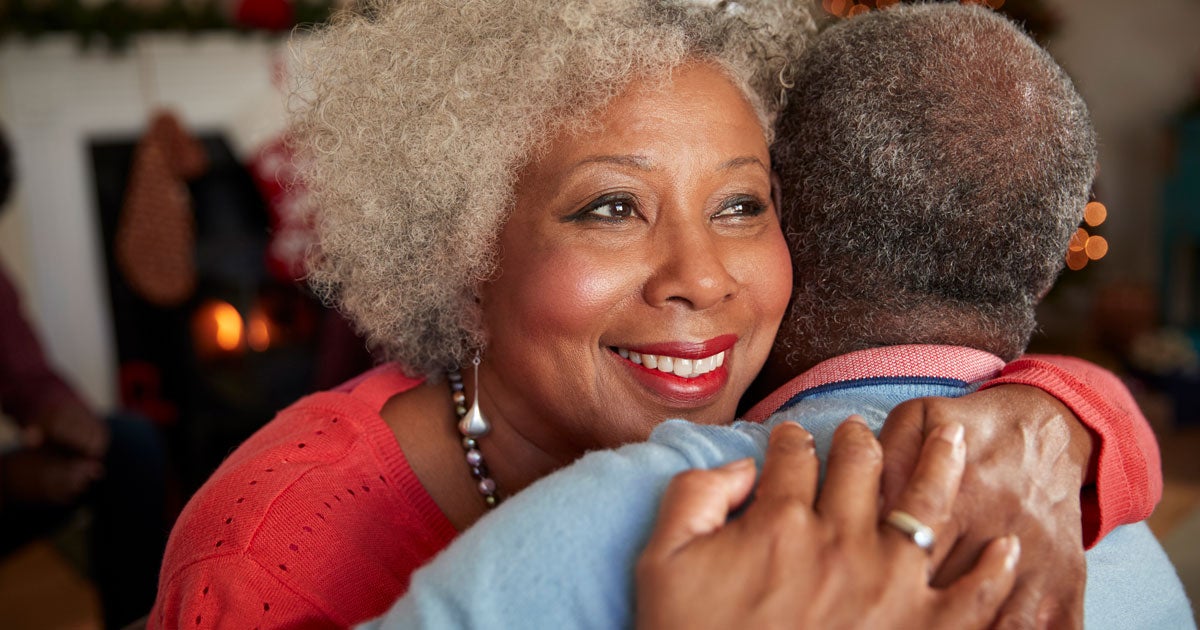 A close up shot of a Black senior woman smiling as she hugs her companion.