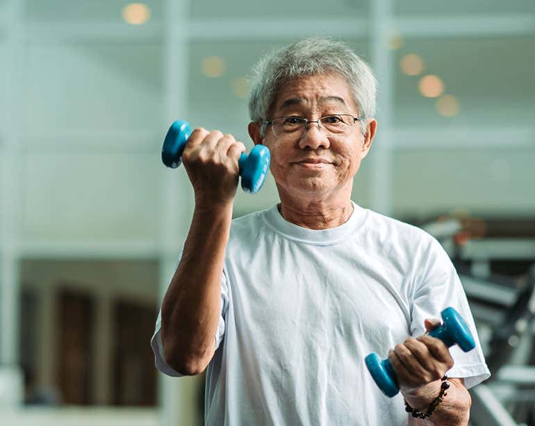 A senior Asian man is seen lifting weights in the gym.