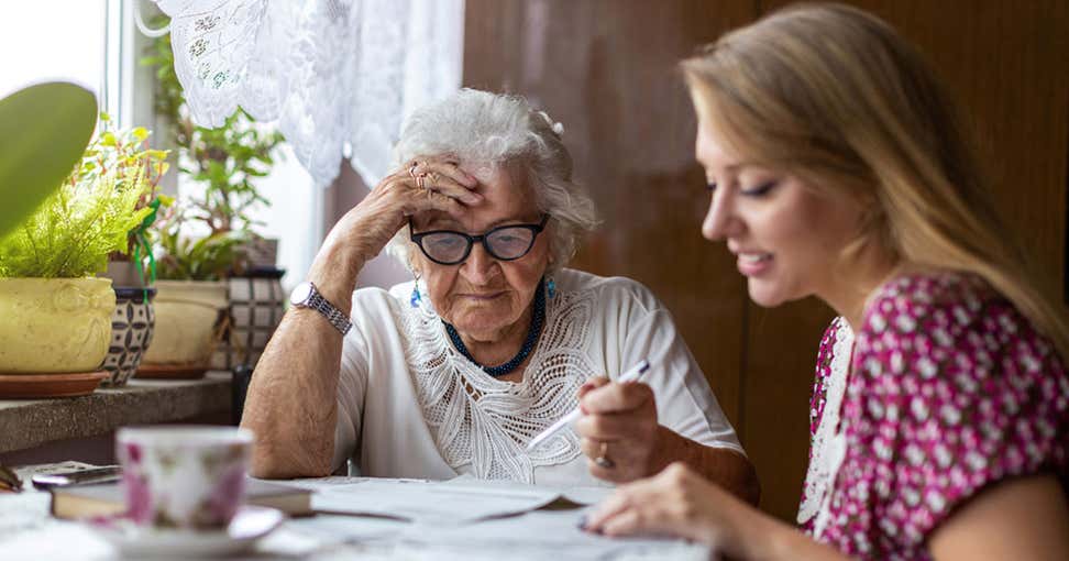 A young female caregiver helps her grandmother with her financial paperwork.