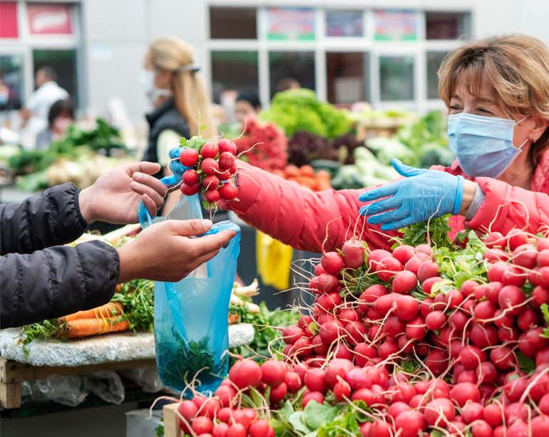 A senior woman is seen shopping for radishes at an outdoor market.