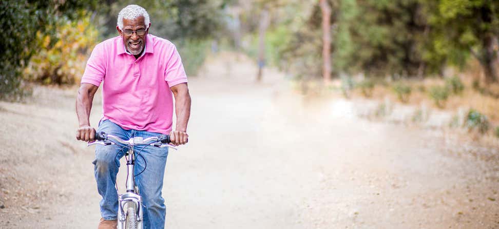 An older black man is riding his bike, laughing and enjoying nature.