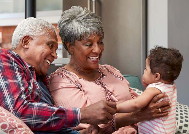 An African American senior couple is sitting on the couch, doting on their grandchild. 
