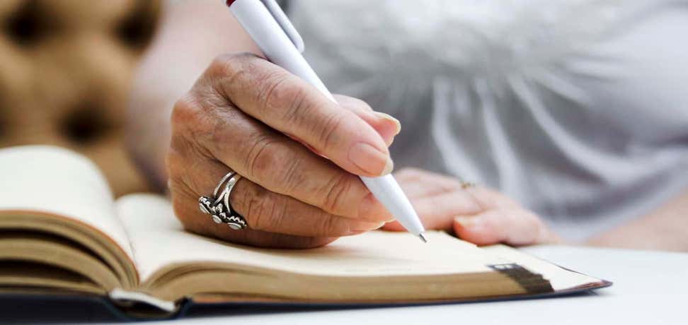 A senior woman is writing on an open notebook during a seminar.