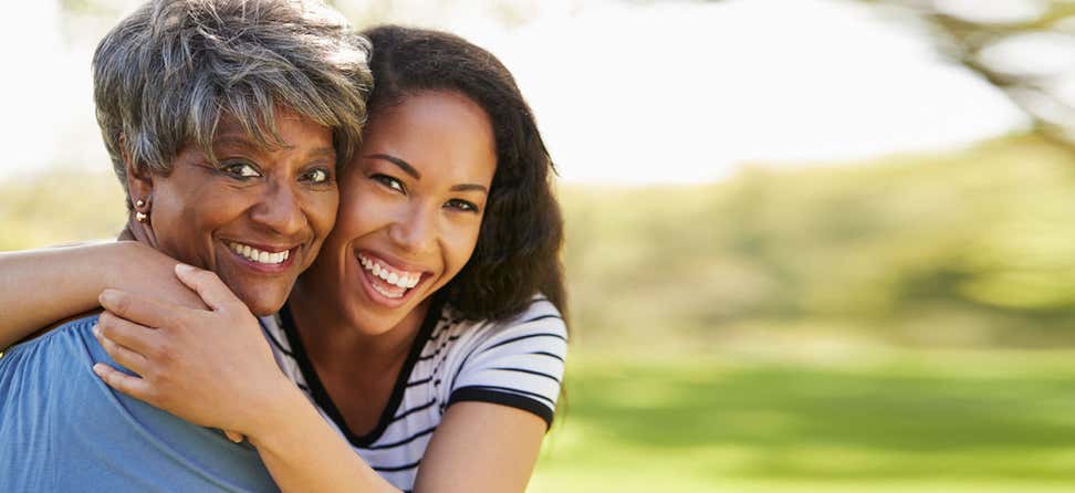 A Black young caregiver is hugging her mom outside in the sun.