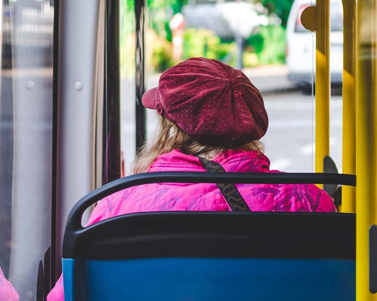 A view from an older woman's back as she sits on a bus.