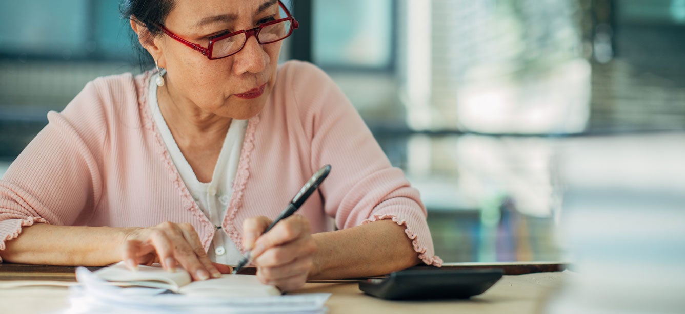 A senior Asian woman is calculating her financials, looking for ways in which she can save in retirement.