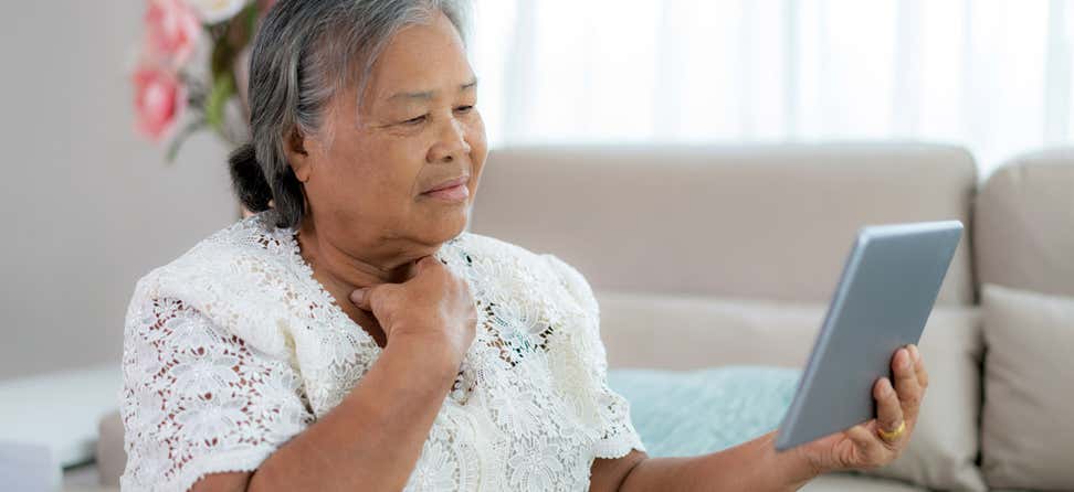 An Asian senior woman is holding her tablet up, making a decision about her health.