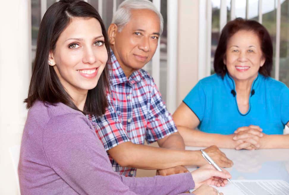Counselor with older Asian couple at table filling out paperwork.