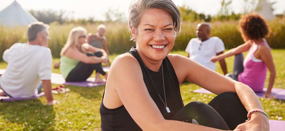 A Black senior woman smiles at the camera while at a yoga retreat with other older adults.