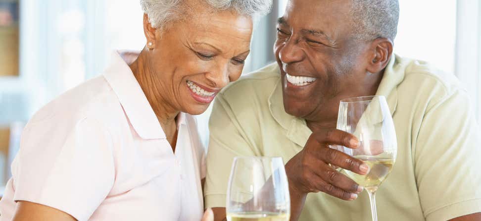 A senior African American couple are laughing while enjoying their wine.