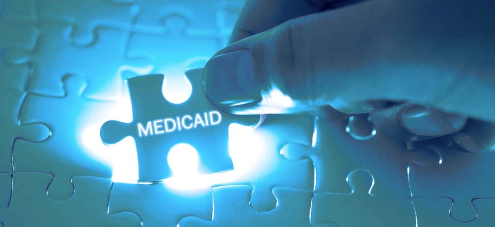 A doctor holds a missing puzzle piece above a large puzzle that says "Medicaid".