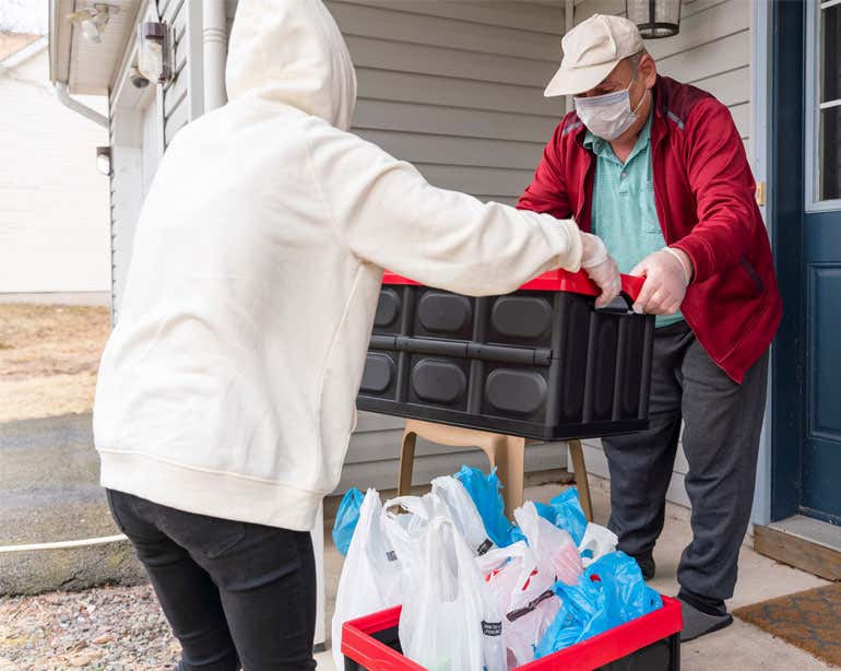 An older man is receiving a grocery delivery at home during the pandemic and is wearing a mask.