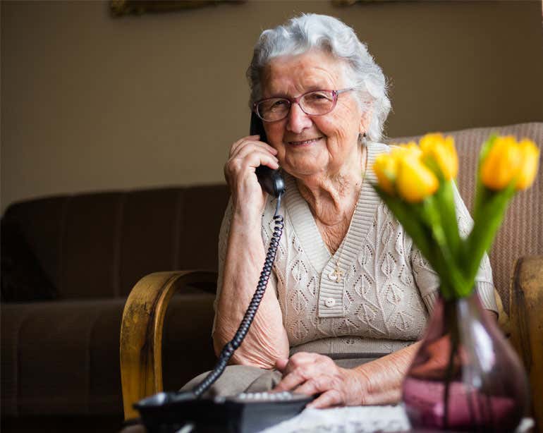 A senior Caucasian woman is smiling while talking on the phone in her home.