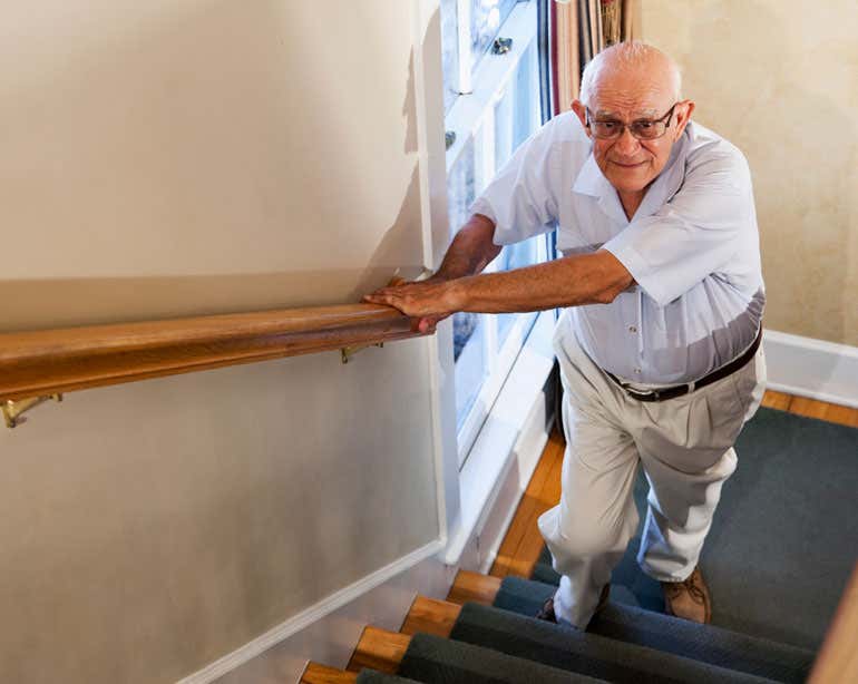 A senior Caucasian man is looking up while he's making an attempt to walk upstairs.