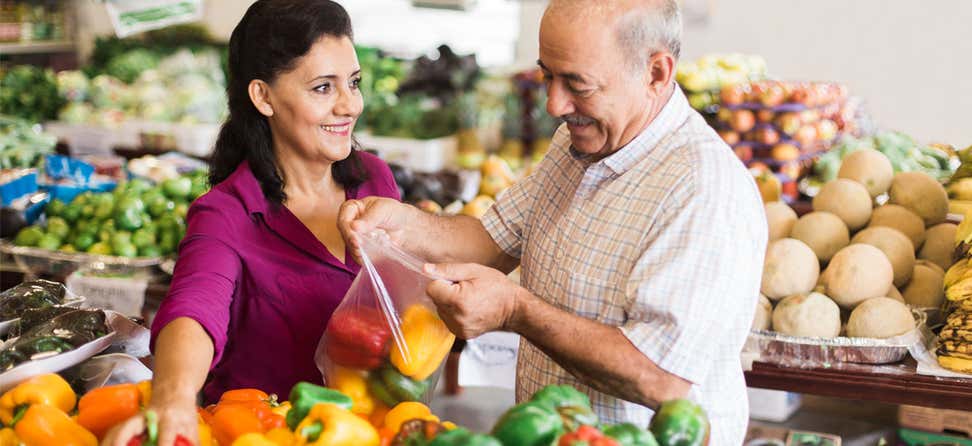Older Hispanic couple is putting bell peppers into bag at grocery store together.
