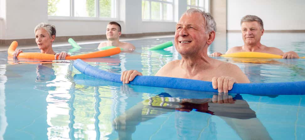 A group of seniors are in a pool doing water aerobics together to improve health and reduce injury.