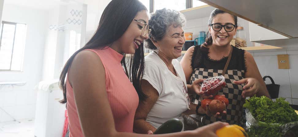 An older hispanic woman unpacks groceries with her daughter and granddaughter in the kitchen.